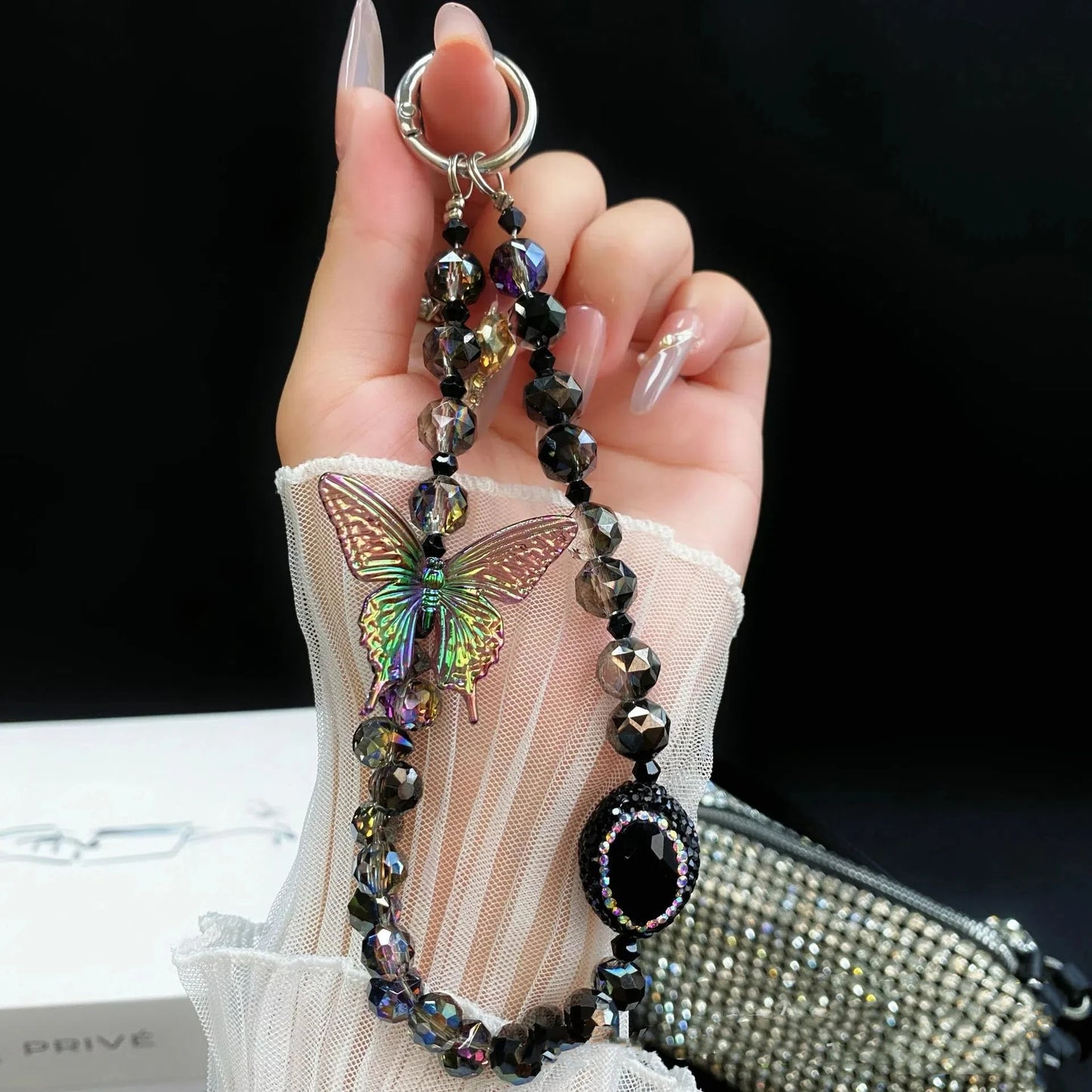 Oppo Reno 14 5G Hand holding a beaded keychain with a butterfly design against a dark background