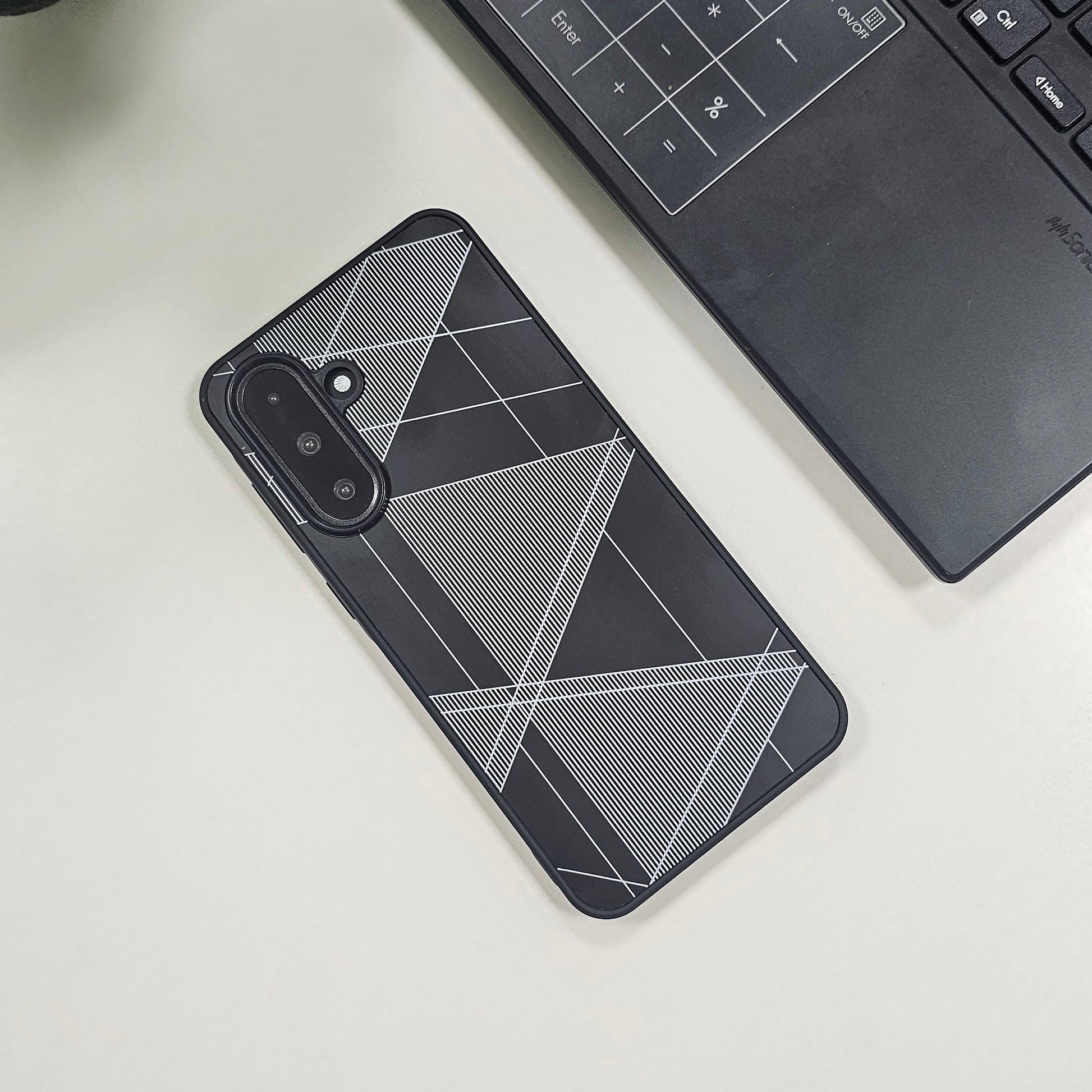 Phone case with geometric design on a light surface next to a laptop