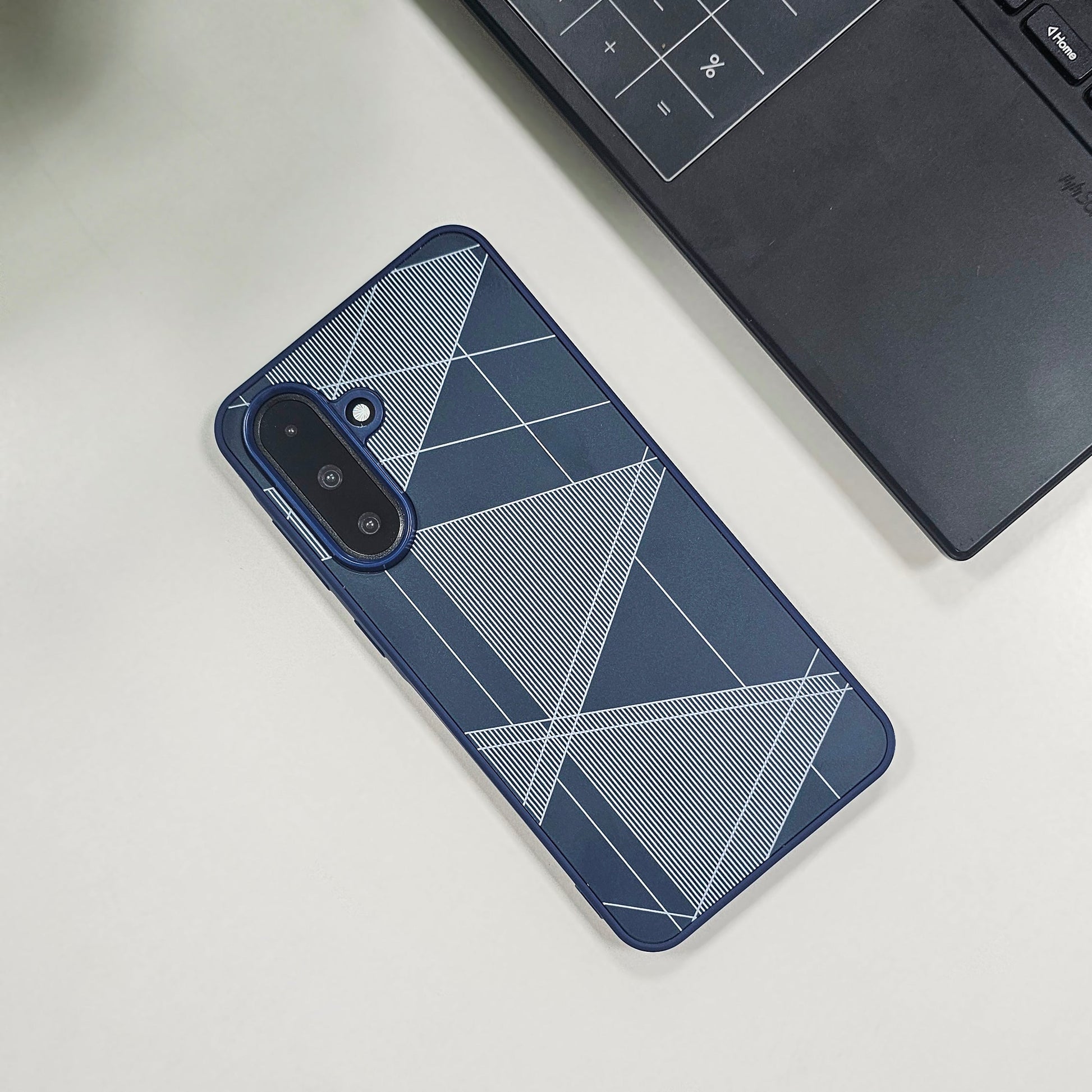 Phone case with geometric design on a light surface next to a laptop