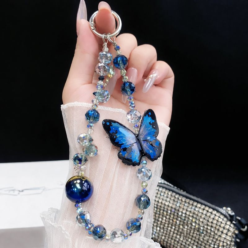 Hand holding a decorative keychain with blue butterfly and beads against a black background